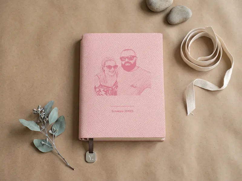 A Blush notebook engraved with a portrait above a caption, on brown kraft paper beside cotton ribbon and dried eucalyptus.
