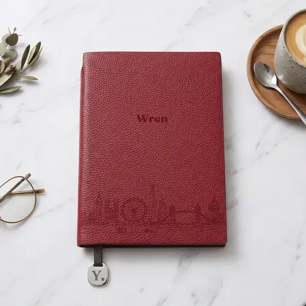 A personalised, laser-engraved A5 notebook on a marble cafe table, beside a flat white in a stoneware cup.