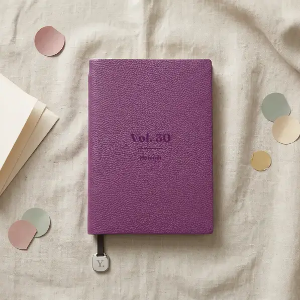 A personalised, laser-engraved A5 notebook on a linen tablecloth, beside a card in its envelope and a scatter of paper confetti.