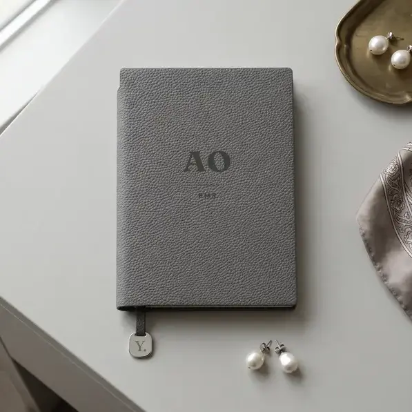 A personalised, laser-engraved A5 notebook on a dressing table, beside a folded silk scarf, a brass tray and pearl earrings.